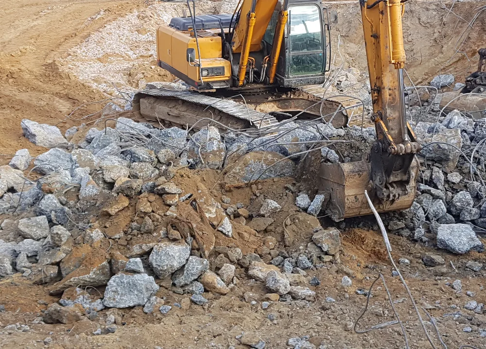 Excavator removing broken concrete slabs